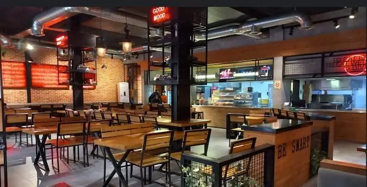 نمای کلی فضای داخلی رستوران آواچی؛ دکوراسیون مدرن و صنعتی با میز و صندلی چوبی، دیوارهای آجری و آشپزخانه باز. محیطی دلنشین و دنج.