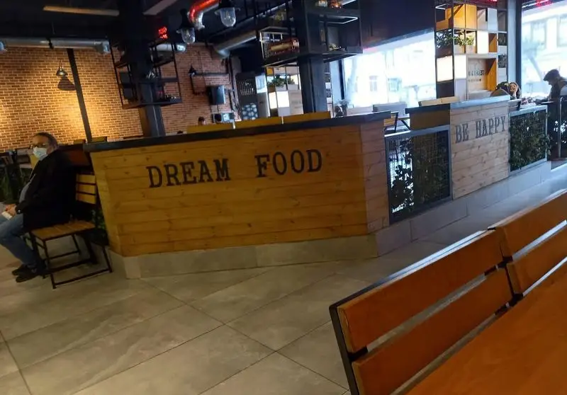 تصویری از فضای داخلی شیک و مدرن رستوران آواچی با دکوراسیون صنعتی، کانتر DREAM FOOD و شعار BE HAPPY، مکانی ایده‌آل برای صرف غذا.