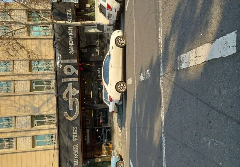 رستوران آواچی: نمایی بیرونی از فست فود آواچی با تابلو "برگر، ساندویچ، پیتزا" در خیابان، با خودروهای پارک شده و ساختمان.