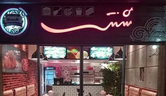 نمای بیرونی فست فود شنتی با تابلوی نئون درخشان، شامل آیکون برگر، مرغ سوخاری و پیتزا. رستورانی با طراحی مدرن و منوی متنوع.