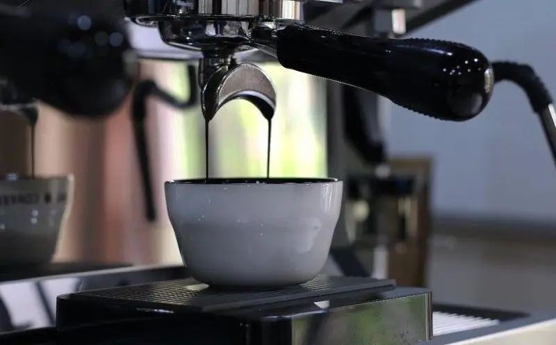 تهیه قهوه اسپرسو تازه و داغ در کافه چکاد، دستگاه حرفه ای در حال پر کردن فنجان. تجربه ای دلنشین از نوشیدنی.