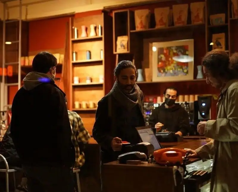 مشتریان در حال تعامل و خرید در کافه چکاد با فضای داخلی دنج و دلنشین، نشان‌دهنده تجربه یک کافه شلوغ.