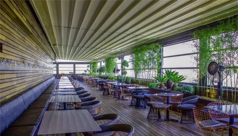 نمایی از فودکورت رویال تراس با سقف متحرک، فضای دنج و مدرن، میز و صندلی‌های شیک، کفپوش چوبی و دکوراسیون سرسبز برای تجربه غذاخوری لذت‌بخش.