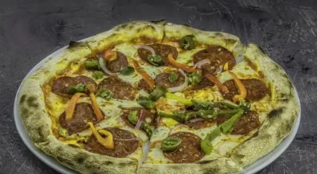 یک پیتزای کامل و اشتهاآور با کراست برشته، پپرونی، فلفل و پیاز قرمز، آماده در فودکورت رویال تراس برای یک تجربه غذایی فوق‌العاده.