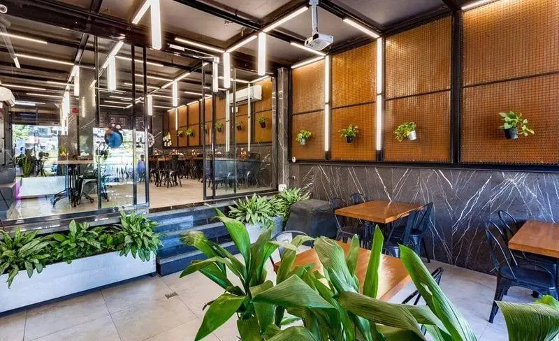 نمایی از فضای داخلی فست فود شیلا: دکوراسیون مدرن، دیوارهای طرح مرمر، گیاهان سبز، میزهای چوبی و نورپردازی جذاب، محیطی دلنشین
