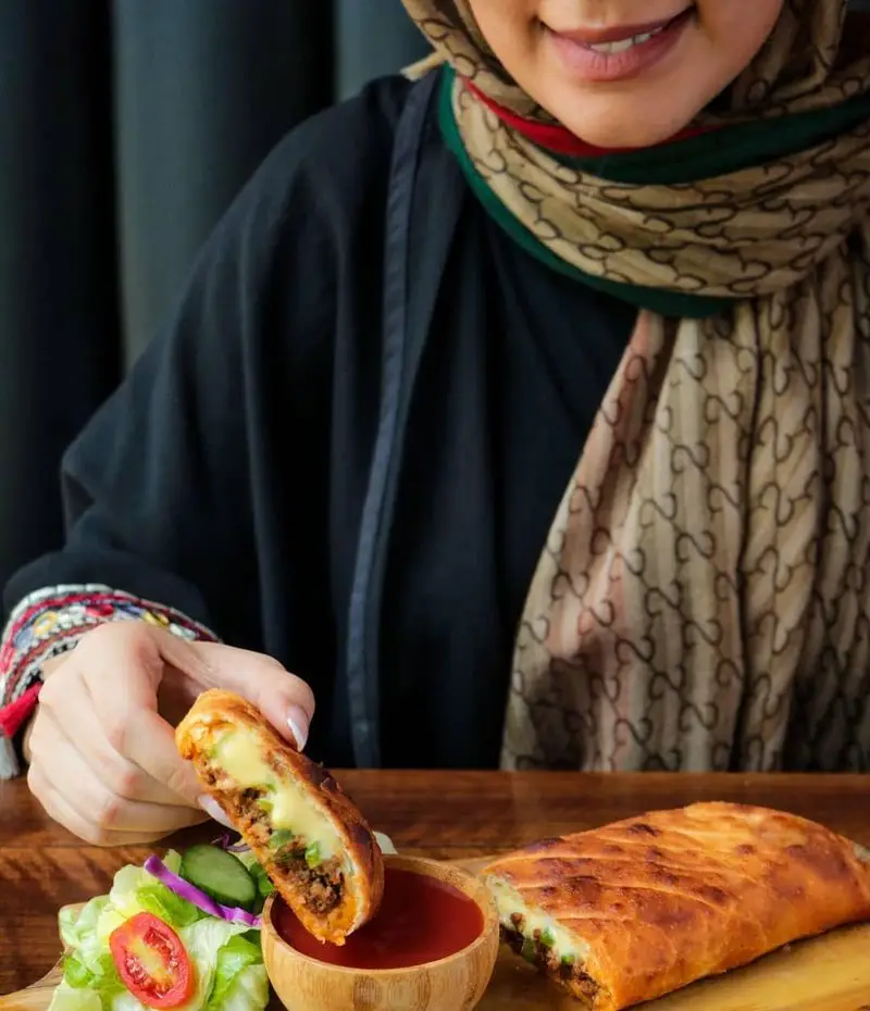 مشتری خوشحال در فست فود شیلا از کالیه گوشت و پنیر طلایی، همراه با سالاد تازه و سس لذیذ، لذت می‌برد.