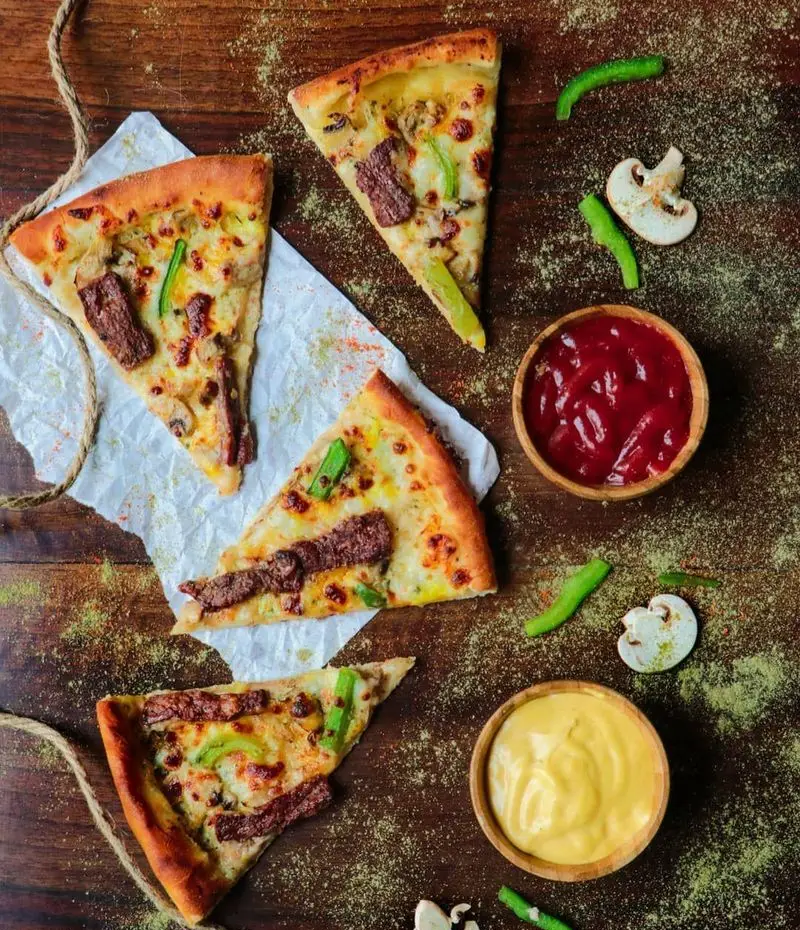 چند برش پیتزا گوشت و قارچ خوشمزه فست فود شیلا با فلفل دلمه‌ای، سس کچاپ و خردل. بهترین پیتزا را از شیلا بخواهید.
