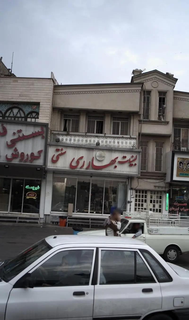 تصویر نمای خیابانی از فروشگاه لبنیات بهارری سنتی با تابلوهای فارسی برجسته و مغازه بستنی کوروش در کنار آن، در محیطی شهری.