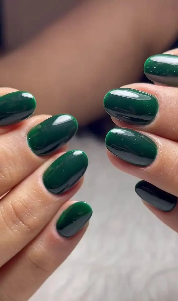 ناخنهای ژلیش سبز تیره و براق با فرم بیضی شیک، نمونه کار کاشت ناخن و ژلیش سالن زیبایی هومیسا برای دستان زیبا.