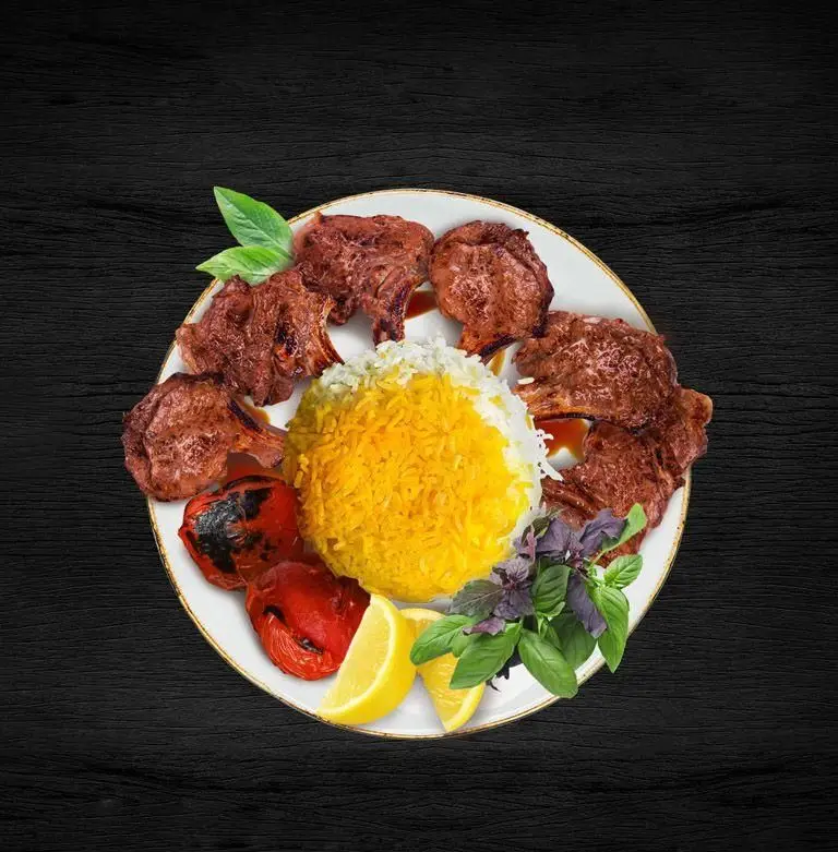 یک پرس شیشلیک خوشمزه رستوران ارکیده (شعبه اقدسیه) شامل دنده کباب، برنج زعفرانی و سفید، گوجه کبابی و لیمو، سرو شده بر روی تخته چوبی.