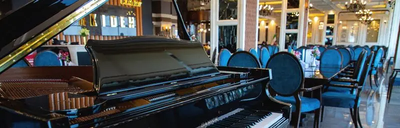 پیانو گرند در فضای داخلی لوکس و شیک رستوران ارکیده شعبه اقدسیه با صندلی‌های آبی، محیطی ایده‌آل برای یک تجربه غذایی بی‌نظیر.