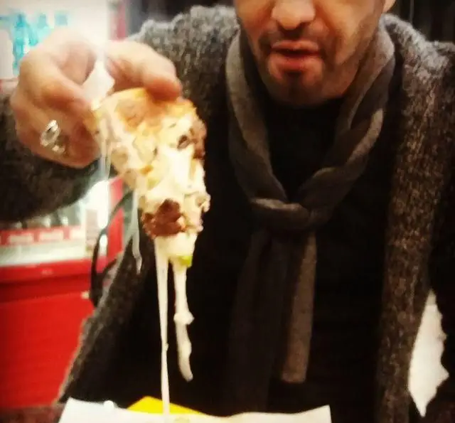 مردی در حال لذت بردن از پیتزای خوشمزه شهر پیتزا با پنیر کش‌دار و لذیذ. تجربه‌ای دلنشین از کیفیت و طعم بی‌نظیر.