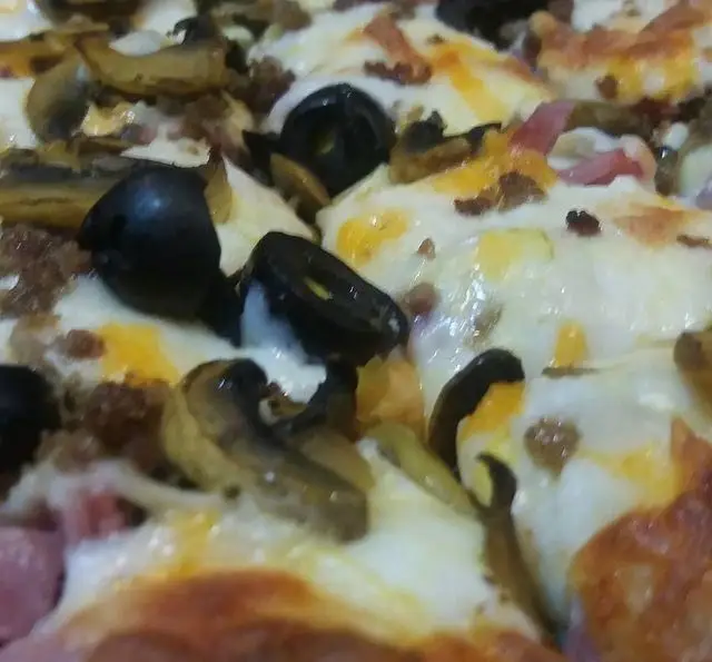 تصویری نزدیک از پیتزا شهر پیتزا با پنیر آب شده، قارچ تازه، زیتون سیاه و گوشت چرخ کرده، یک غذای فست فود خوشمزه.