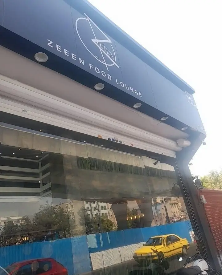 تصویری از نمای بیرونی شیک فست فود زین (ZEEEN FOOD LOUNGE) با لوگوی برجسته، ویترین بزرگ و انعکاس محیط شهری شلوغ.