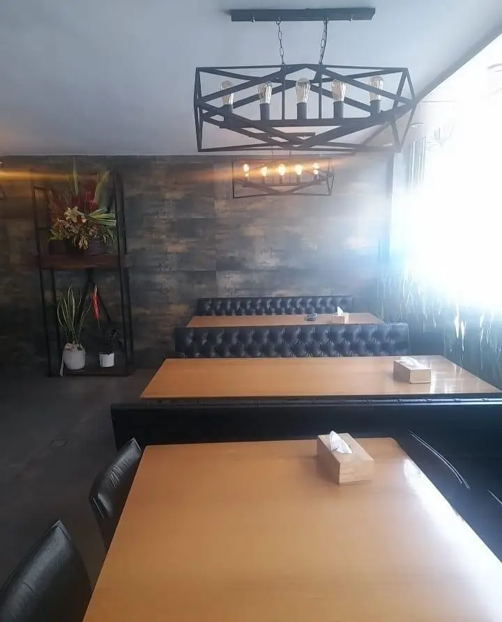 نمایی از دکوراسیون داخلی مدرن و دلنشین فست فود زین، شامل میزهای چوبی روشن، صندلی‌های راحتی و نورپردازی صنعتی شیک. ایده‌آل برای صرف غذا در فست فود زین.