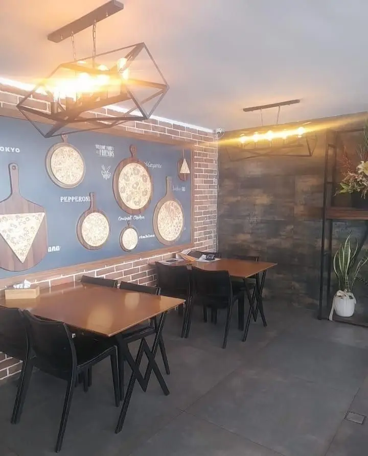 نمای داخلی فست فود زین با نورپردازی گرم، میز و صندلی‌های راحت و دکوراسیون جذاب شامل دیوار آجری و طرح‌های پیتزا.