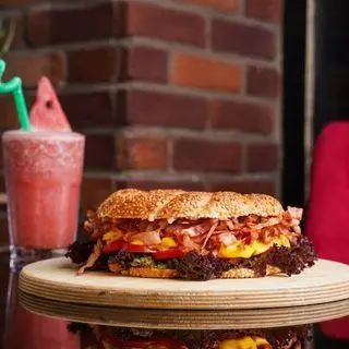 ساندویچ لذیذ و پرملات کافه رستوران عجمان با بیکن، پنیر و سبزیجات تازه، سرو شده با آب هندوانه خنک، انتخابی عالی برای وعده غذایی شما.