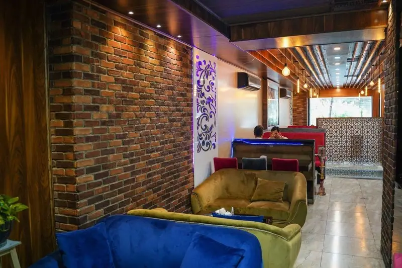 نمایی از دکوراسیون داخلی جذاب و راحت کافه رستوران عجمان، با دیوار آجری، مبلمان متنوع و نورپردازی دلنشین برای مشتریان.