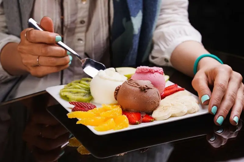 مشتری در کافه رستوران عجمان در حال لذت از دسر خوشمزه بستنی با میوه‌های تازه مانند کیوی، توت فرنگی، موز و پرتقال.