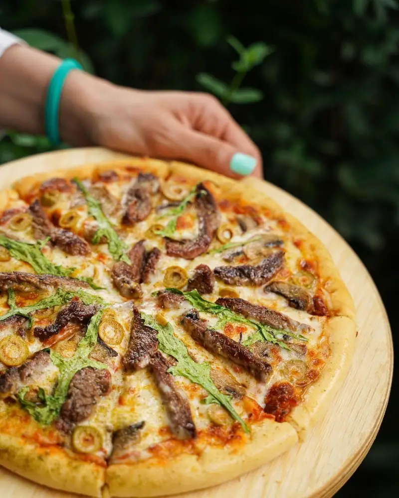 پیتزا گوشت و قارچ با زیتون و سبزیجات تازه از کافه رستوران عجمان. طعمی بی‌نظیر برای ناهار یا شام شما.