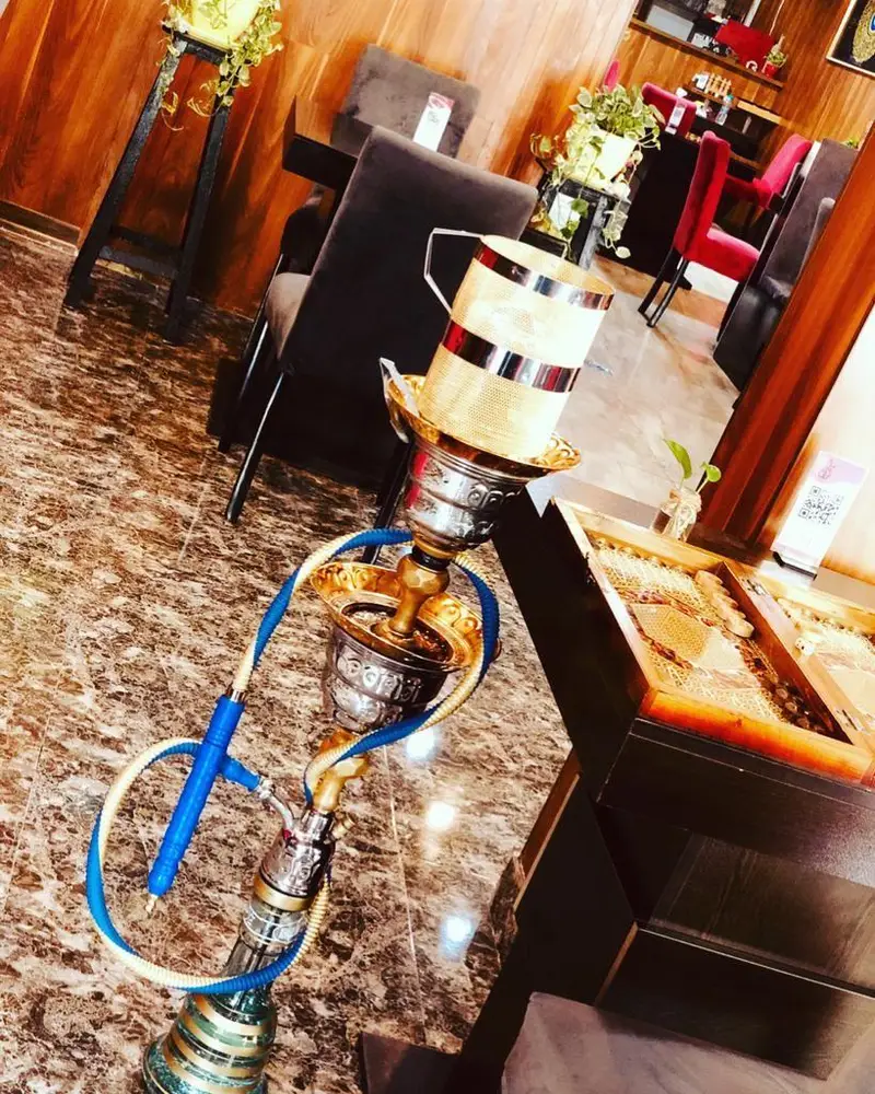 تصویری از قلیان شیک در کافه رستوران عجمان، با فضای گرم و دلنشین، میز و صندلی‌های راحت و دکوراسیون چوبی.