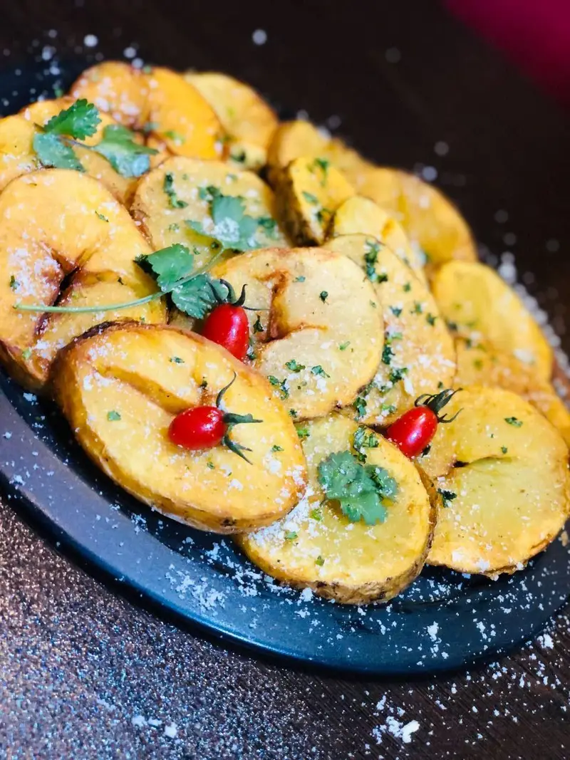 سیب زمینی ورقه ای طلایی و خوش طعم با پنیر پارمزان، سبزی معطر و گوجه گیلاسی در کافه رستوران عجمان. لذیذ و دلپذیر.