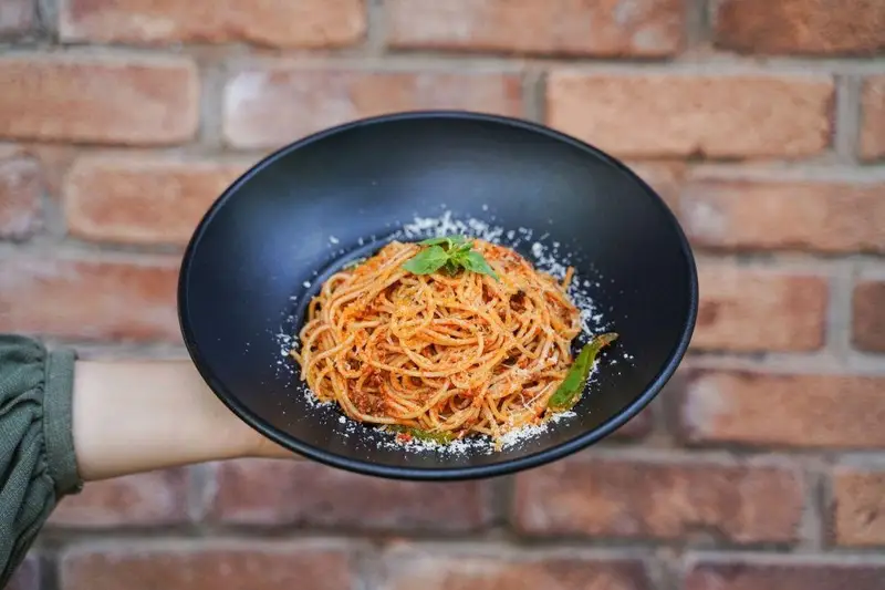 تصویری جذاب از اسپاگتی بولونیز خوشمزه با پنیر پارمزان و ریحان، آماده سرو در کافه رستوران عجمان، مناسب وعده ناهار یا شام.