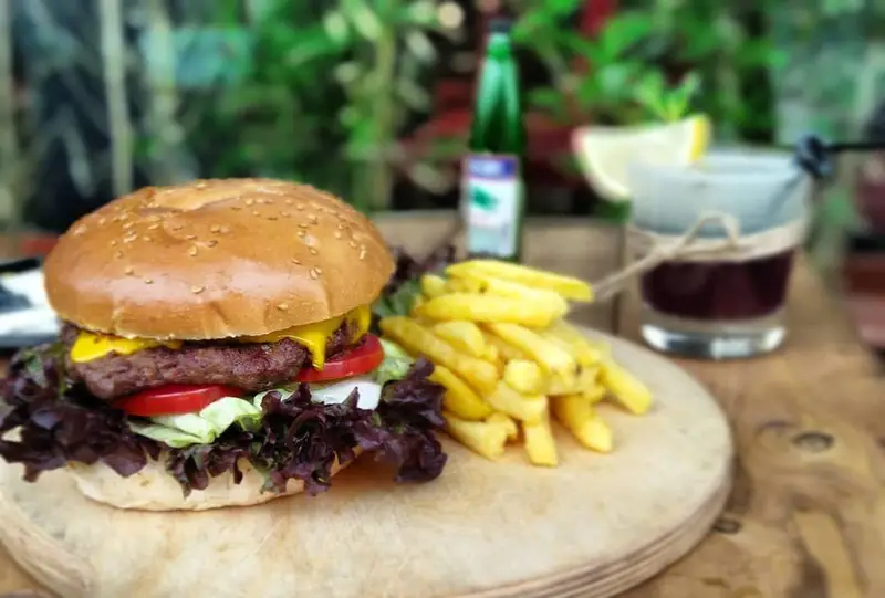 همبرگر پنیر با سس، کاهو و گوجه فرنگی، در کنار سیب زمینی سرخ کرده طلایی و نوشیدنی خنک در کافه رستوران عجمان. تجربه‌ای دلپذیر.