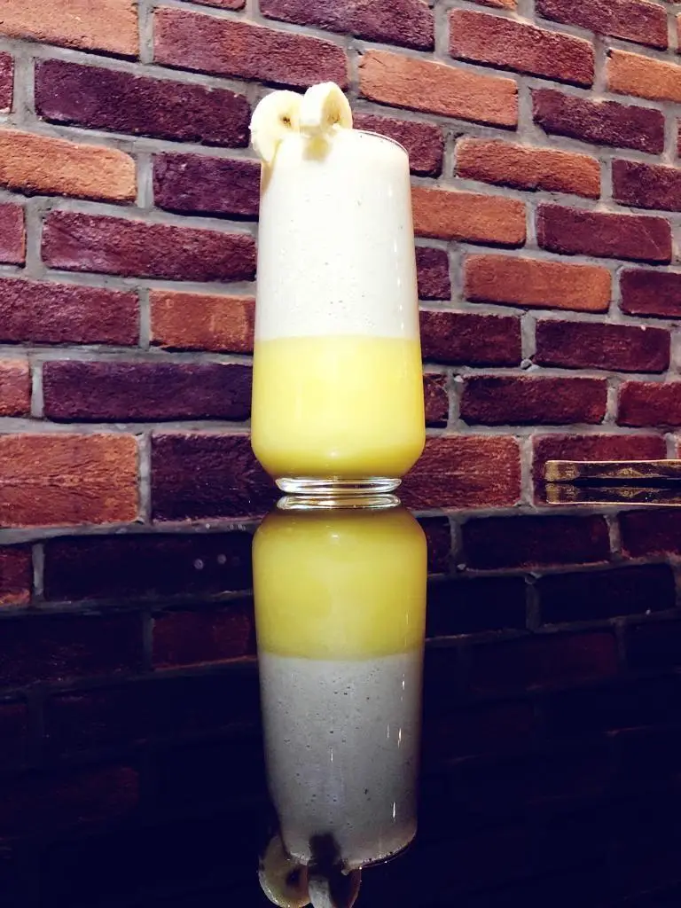 اسموتی دو لایه موز و میوه های استوایی، نوشیدنی خنک و دلپذیر کافه رستوران عجمان، مناسب برای روزهای گرم.