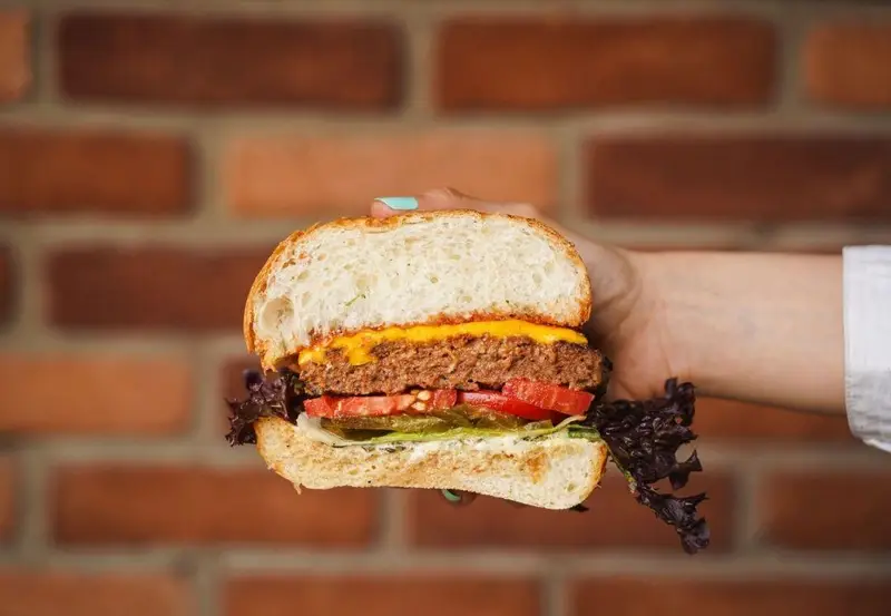 برگر تازه و اشتهاآور با برش نیمه، نمایش لایه‌های پنیر ذوب شده، پتی، گوجه و کاهو، آماده سرو در کافه رستوران عجمان.