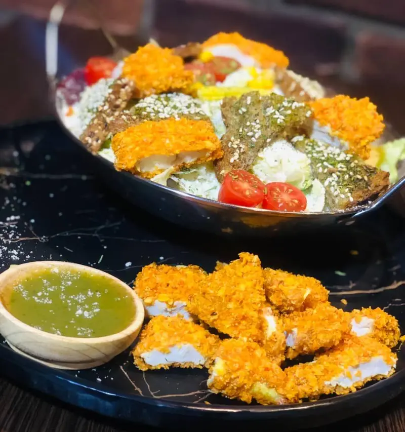 سالاد متنوع با تکه‌های سوخاری مرغ یا ماهی و سس سبز در کافه رستوران عجمان. منوی جذاب و خوشمزه برای لحظاتی دلنشین.