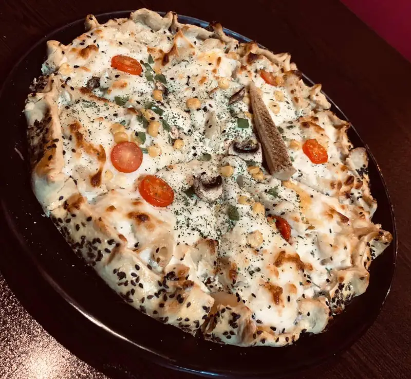 پیتزا خاص کافه رستوران عجمان با سس سفید، قارچ، ذرت و گوجه گیلاسی. یک غذای خوشمزه و متفاوت با لبه نان کنجدی، مناسب شام و ناهار.