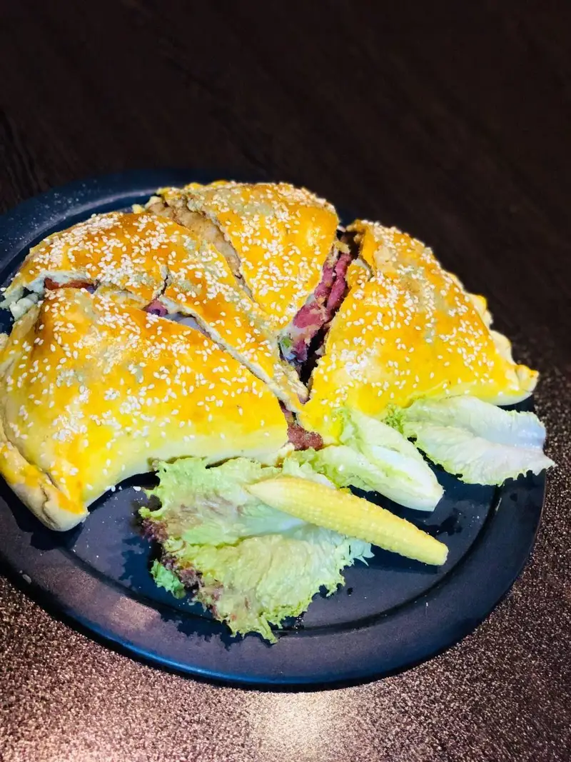 پیتزا کالزونه بزرگ با فیلینگ گوشت و پنیر، خمیر طلایی کنجدی، همراه با سالاد و بیبی کورن در کافه رستوران عجمان.