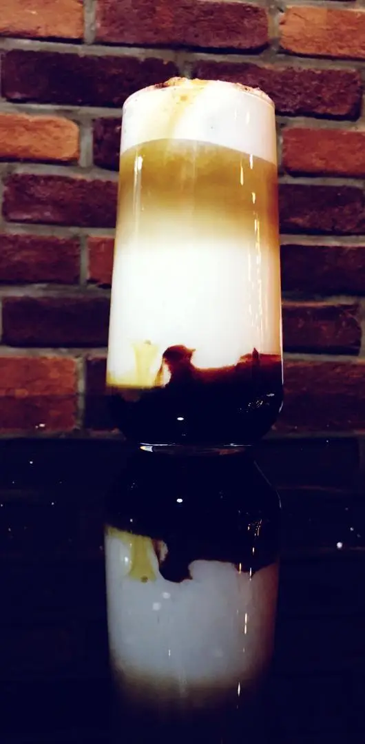 نوشیدنی لایه ای جذاب و خوشمزه کافه رستوران عجمان شامل شیر، قهوه و شکلات با فوم غلیظ روی آن، تجربه ای دلنشین در کافه