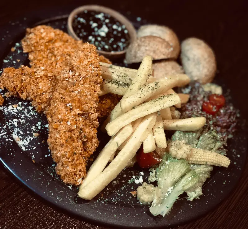 نمایی اشتهاآور از استریپس مرغ کریسپی، سیب زمینی سرخ کرده، سس مخصوص و سالاد تازه در کافه رستوران عجمان.