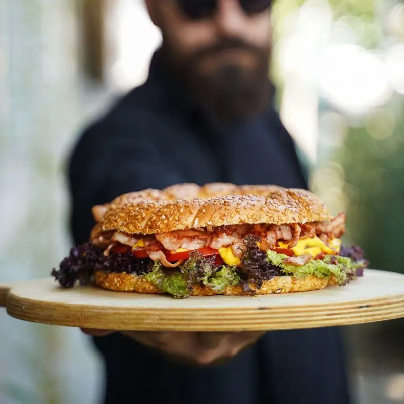 همبرگر بزرگ و لذیذ بیکن با کاهو و گوجه فرنگی، سرو شده بر تخته چوبی در کافه رستوران عجمان، تجربه ای فراموش نشدنی.