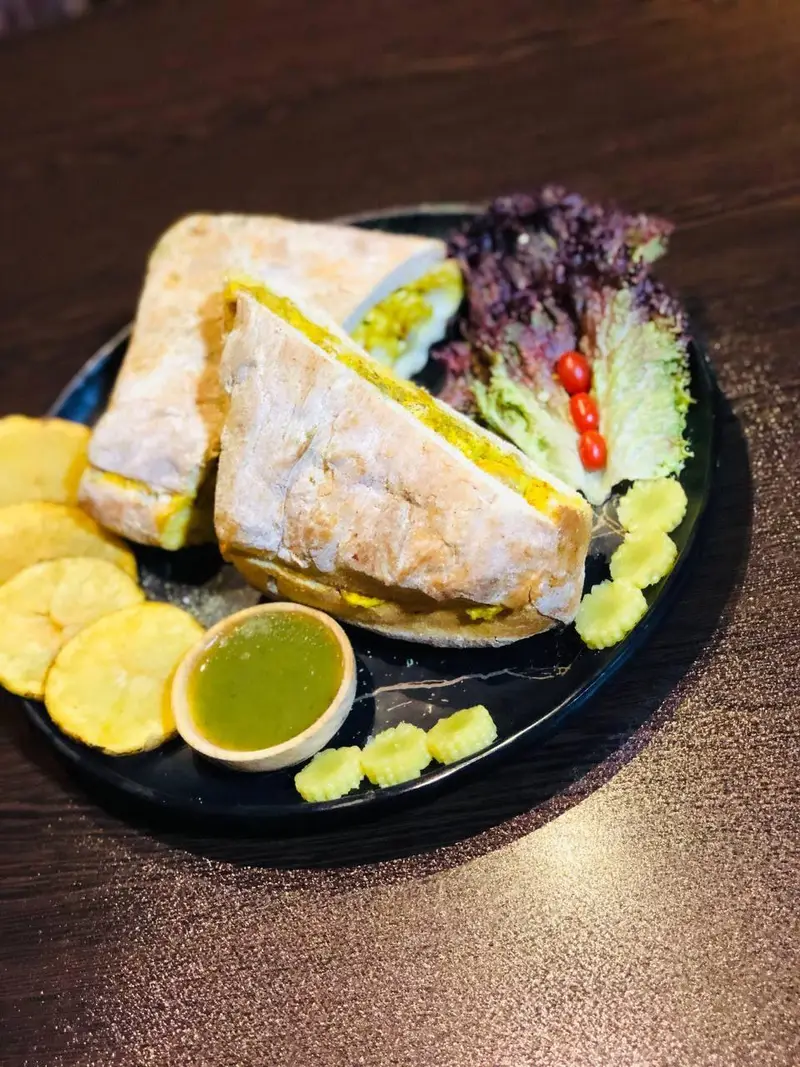 ساندویچ مخصوص کافه رستوران عجمان همراه با سالاد رنگارنگ، چیپس طلایی و سس چاتنی خوش طعم. یک وعده غذایی عالی و کامل.