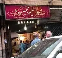 تابلوی قرمز رنگ و شلوغی ورودی مغازه حلیم و کباب مجید، مشتریانی که برای تجربه طعم اصیل و سنتی حلیم و کباب به این مکان آمدهاند.