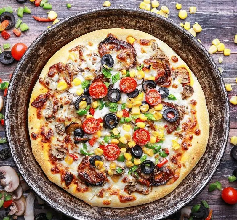 تصویری زیبا از پیتزا سبزیجات تازه و خوشمزه با قارچ، ذرت، زیتون، گوجه و فلفل در سینی فلزی. ارائه شده توسط برگر زغالی قیطریه.