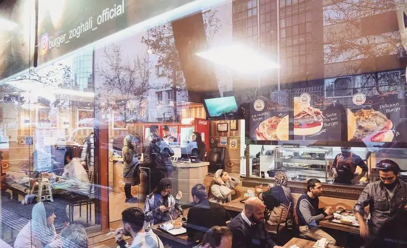 نمای پرتردد و دلنشین رستوران برگر زغالی قیطریه در تهران، با مشتریان در حال صرف همبرگرهای لذیذ و باکیفیت.