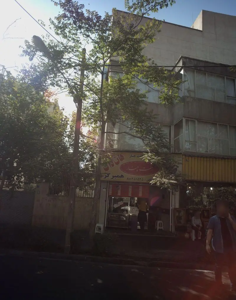 فست فود هفت چنار در تهران، نمای بیرونی مغازه با تابلوی شامل نام، شماره تلفن ۸۸۳۵۱۵۲۵ و کلمه همبرگر. فضای سبز و خیابان.