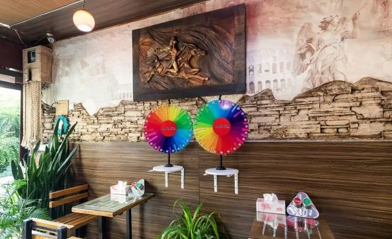 دکوراسیون داخلی پیتزا پنجره شامل دیوار آجری، نقاشی رومی، دو چرخ شانس رنگی، میز و صندلی چوبی و فضای سبز دلنشین.