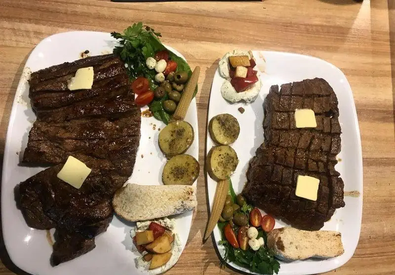 دو بشقاب استیک لذیذ کافه رستوران مکث با مخلفاتی چون سیب‌زمینی، زیتون، گوجه و کره روی گوشت، تجربه‌ای عالی از طعم و کیفیت.