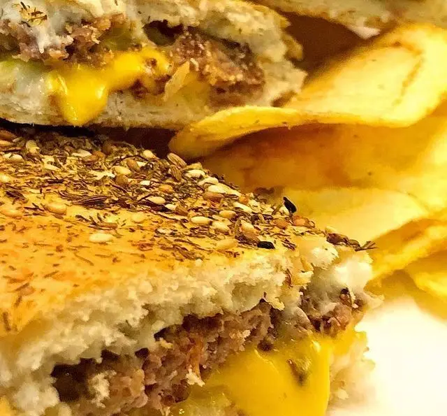 ساندویچ برگر لذیذ کافه رستوران مکث با پنیر طلایی آب شده، چاشنی معطر روی نان و چیپس ترد، انتخابی عالی برای یک وعده خوشمزه.