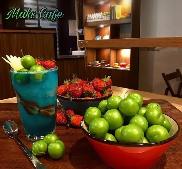 نوشیدنی خنک آبی با توت فرنگی و گوجه سبز در کافه رستوران مکث، همراه با ظرف‌های میوه تازه روی میز چوبی دکور شده.