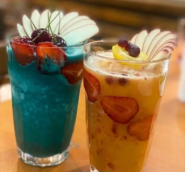 دو نوشیدنی میوه‌ای تازه و جذاب از کافه رستوران مکث: اسموتی آبی با توت فرنگی، گیلاس و سیب، و آبمیوه پرتقالی با توت فرنگی و لیمو.