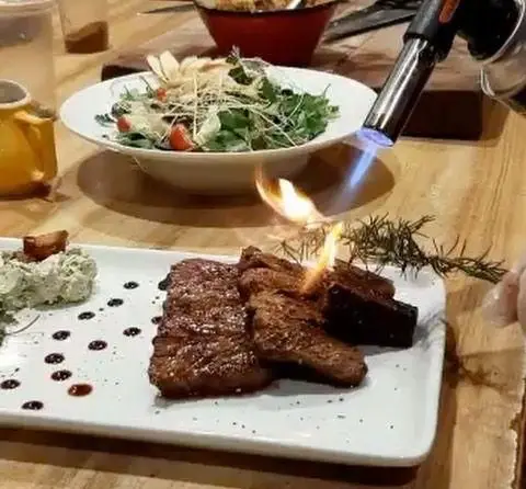 استیک‌های گریل شده کافه رستوران مکث: طعم و عطر بی‌نظیر با فندک آشپزی و رزماری شعله‌ور در کنار سالاد تازه و سس مخصوص.