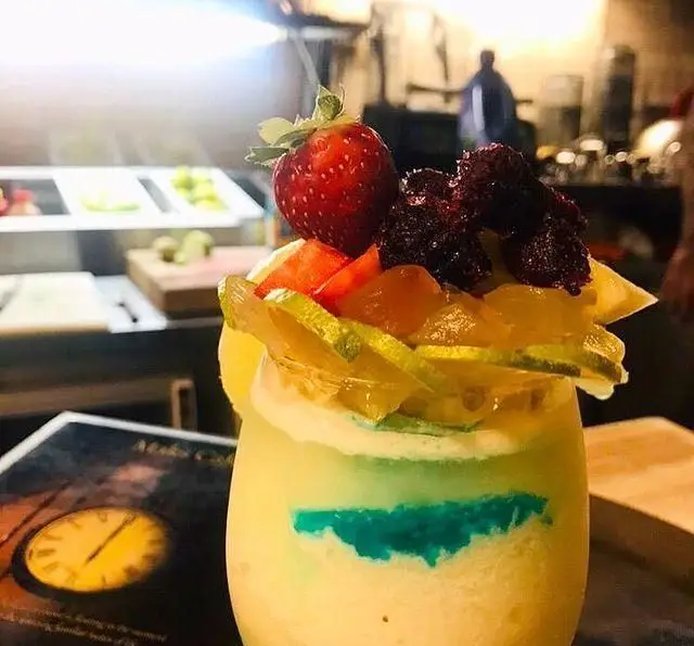 اسموتی میوه‌ای تازه و رنگارنگ کافه رستوران مکث با توت فرنگی، توت سیاه، برش‌های لیمو و لایه آبی خاص، آماده سرو.