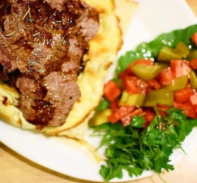 تصویری از غذای جذاب کافه رستوران مکث: برش‌های گوشت طعم‌دار با سس، روی نان تازه، و سالاد سبز و قرمز اشتها‌آور در کنار.