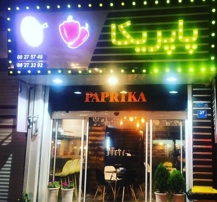 تصویری از نمای شبانه فست فود پاپريكا با تابلوهای نئونی درخشان، لوگوهای فلفل دلمه‌ای و شماره تماس‌ها: 88275749 و 88273392.
